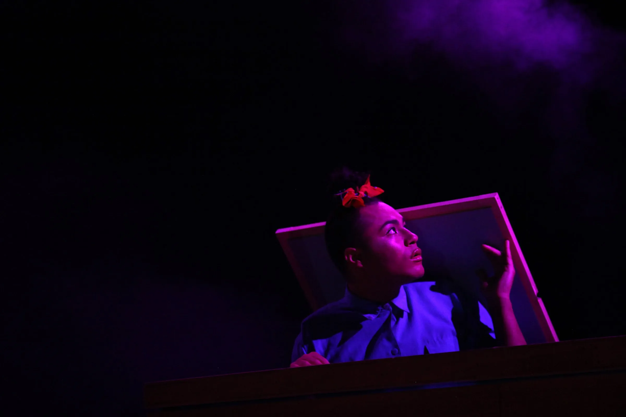 Travis Alabanza peers out from a tilted frame in purple light