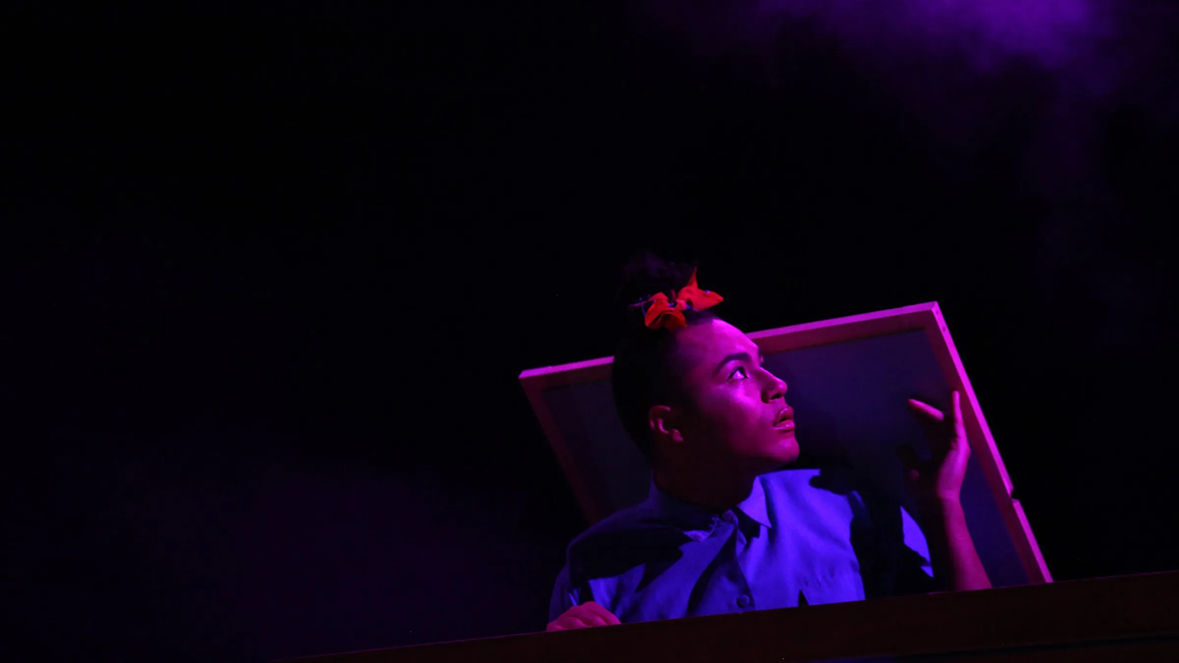Travis Alabanza peers out from a tilted frame in purple light