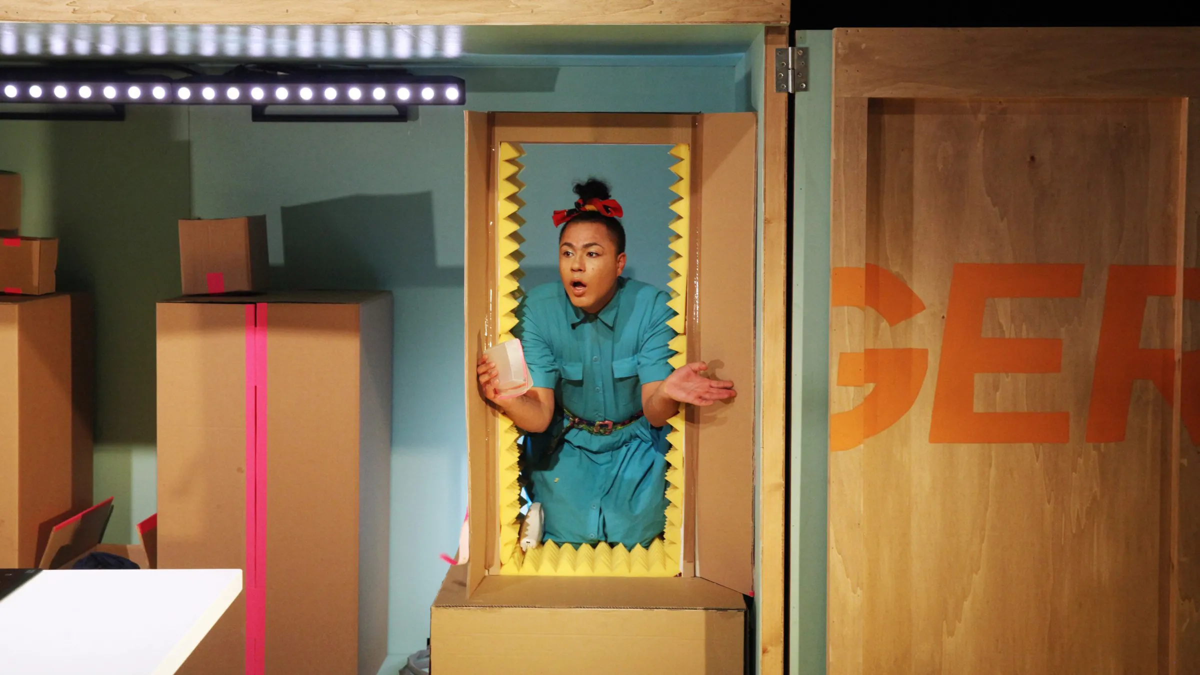 Travis Alabanza in a cardboard box doorway on the set