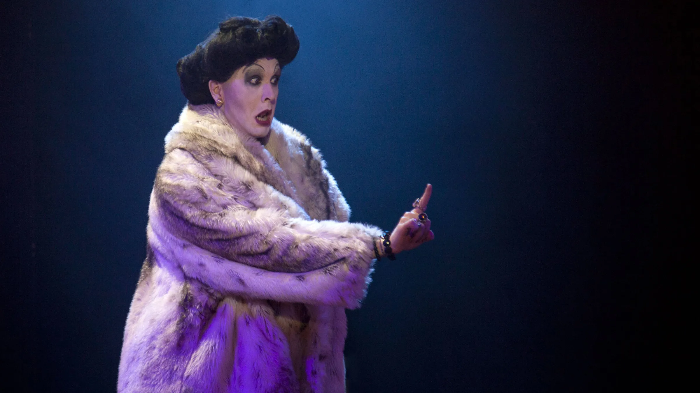 Peter Clements as Frau Welt in a fur coat raising a finger